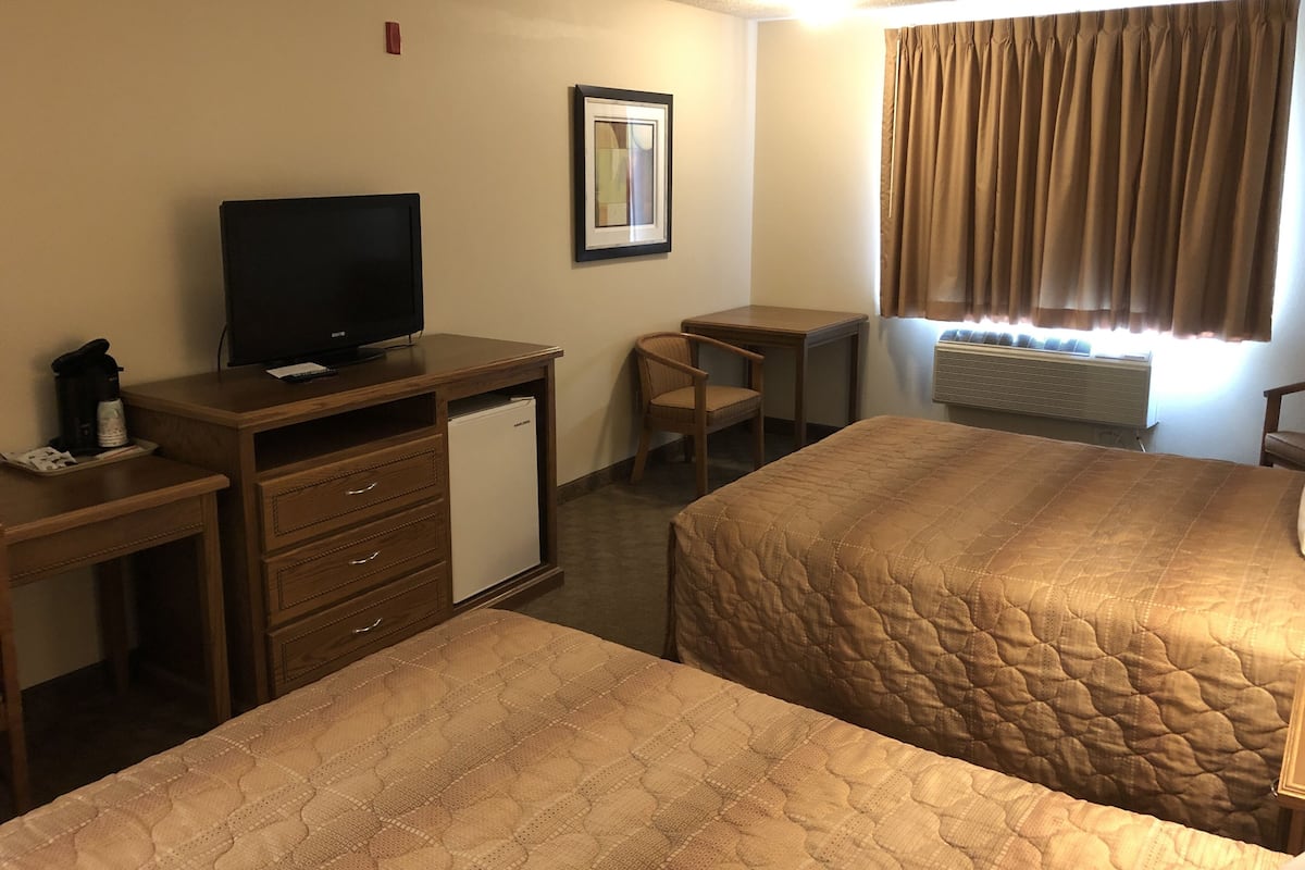 A hotel room with two beds, a desk with a television, a chair, a small refrigerator, and a window with curtains.