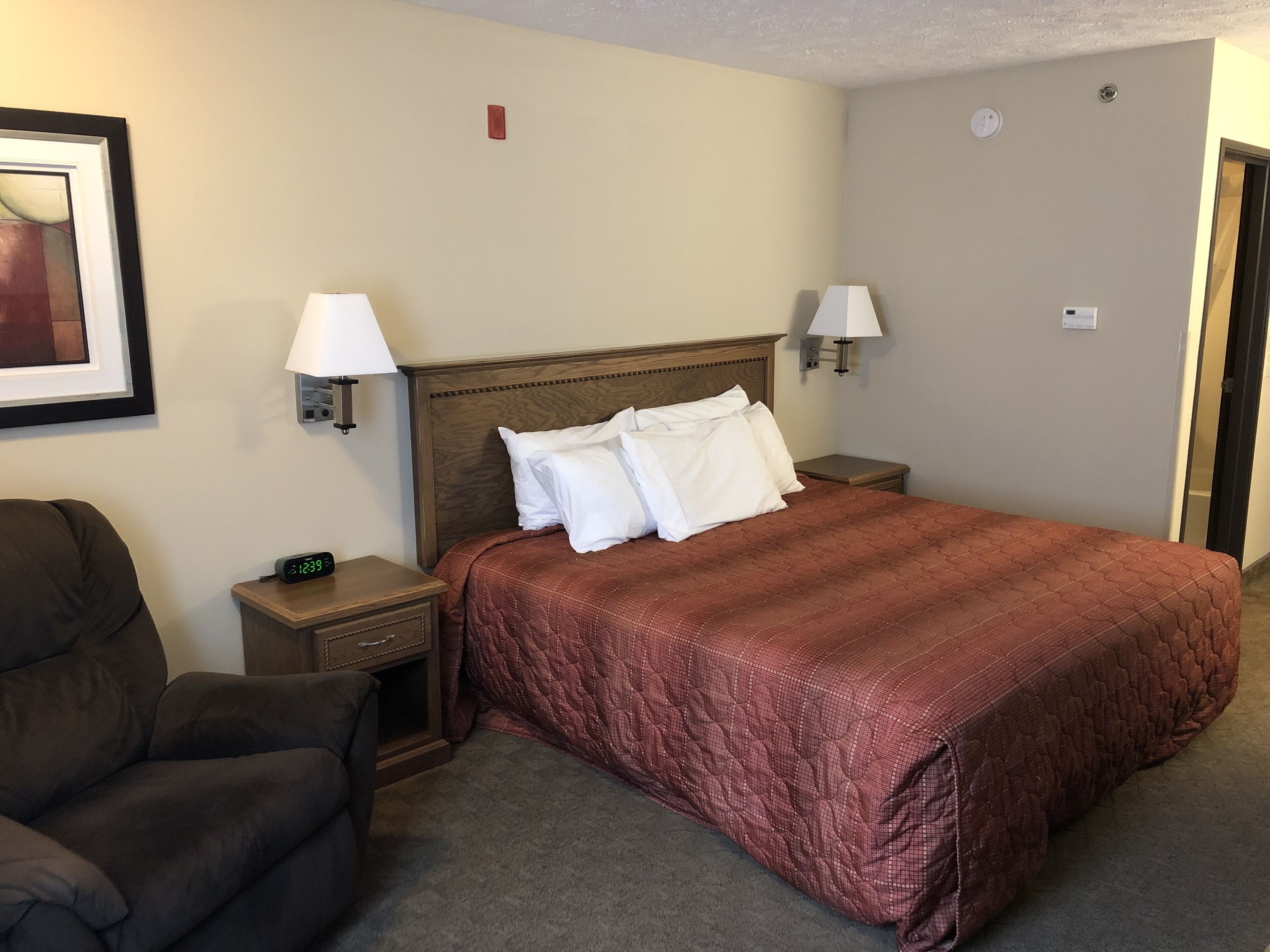 A hotel room with a large bed, two bedside lamps, a nightstand, a chair, and a framed picture on the wall.
