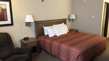 A hotel room with a large bed, two bedside lamps, a nightstand, a chair, and a framed picture on the wall.