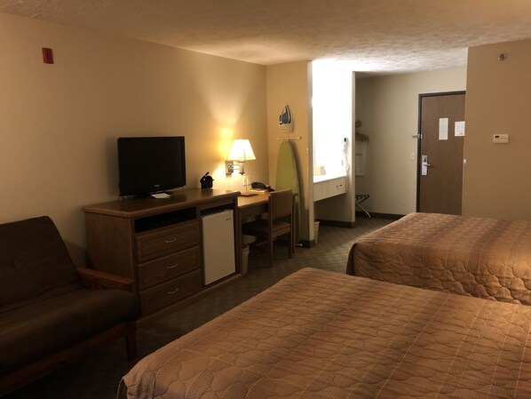 A hotel room with two beds, a desk with a television, a lamp, and a mirror.