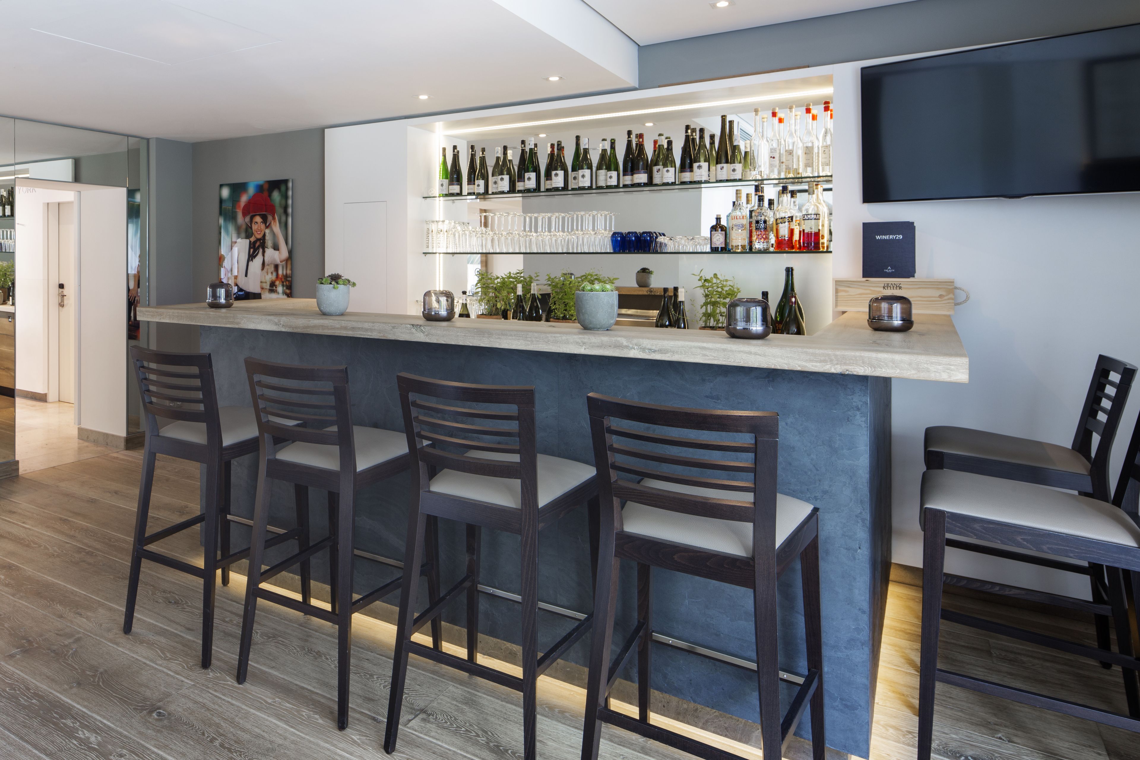 A modern bar area with a long counter, multiple stools, and a variety of bottles and glasses.