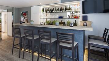 A modern bar area with a long counter, multiple stools, and a variety of bottles and glasses.