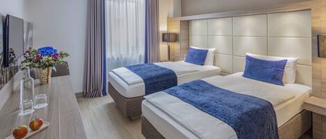A hotel room with two beds, a desk with a vase of flowers, and a large window with curtains.