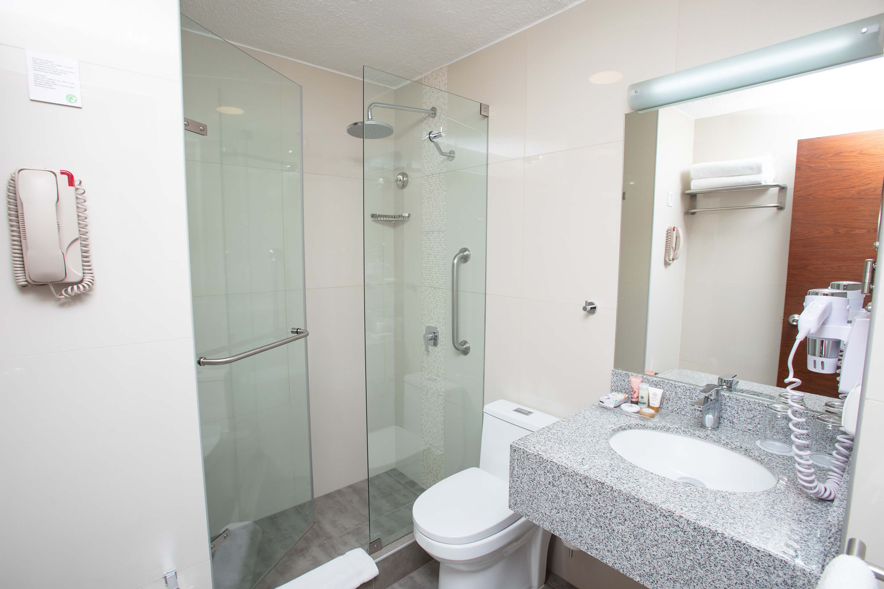 Une salle de bain moderne avec une douche à parois de verre, des toilettes blanches et un lavabo surmonté d’un plan de travail en granit.