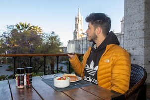 A person sitting at a wooden table with a meal and condiments, overlooking a historic building with a church spire.