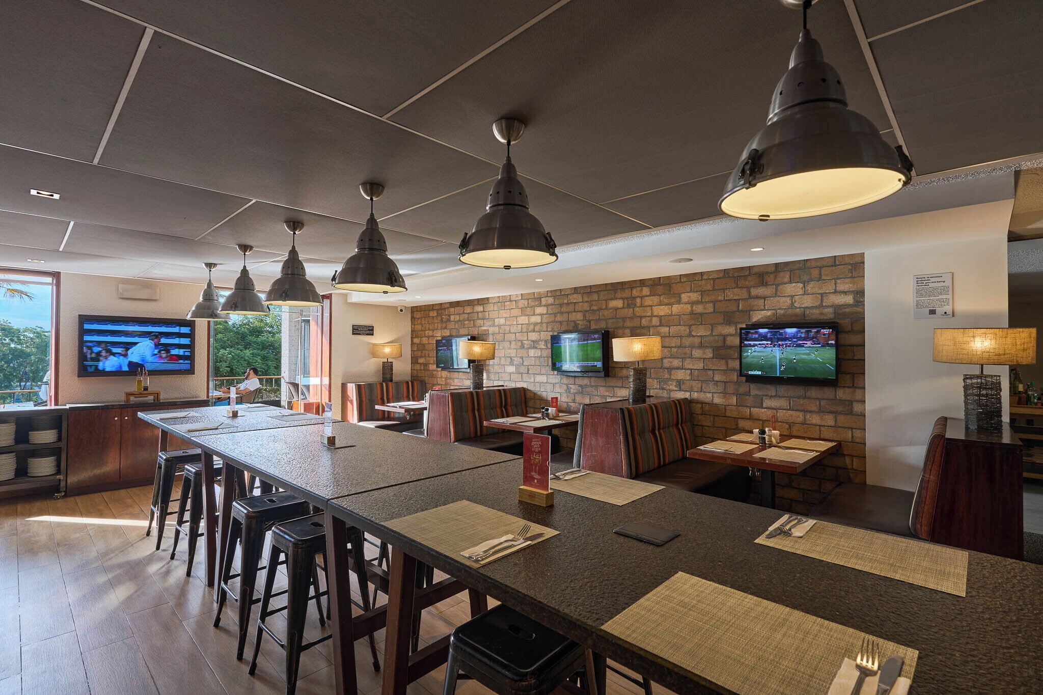 A restaurant with a long communal table, booths, and bar seating. There are multiple televisions mounted on the walls.