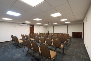 Un salón de conferencias con filas de sillas, luces en el techo y un equipo de aire acondicionado.