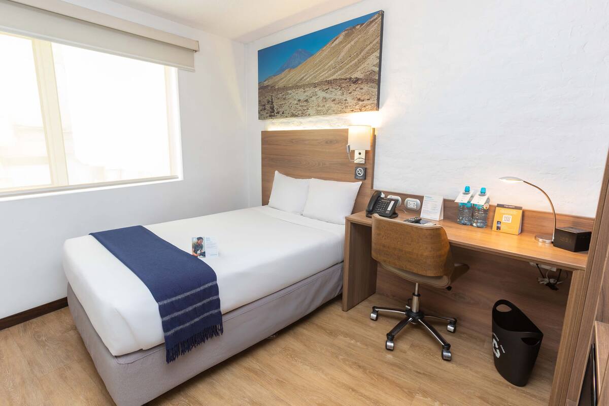Ein Hotelzimmer mit Bett, Schreibtisch, Stuhl und einem Bild an der Wand.