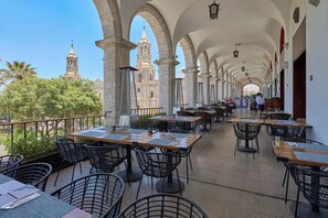 Een terras met tafels en stoelen, met uitzicht op een kerk met een klokkentoren, en een helderblauwe lucht.