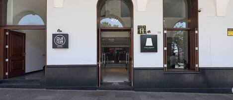 Entrada de um edifício com portas arqueadas, uma placa com 'Plaza Casa Andina' e o número '116' visível.