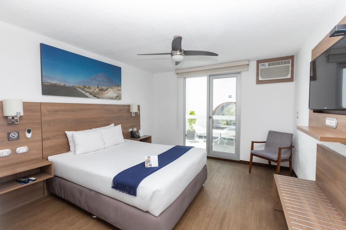 Ein Hotelzimmer mit einem Bett, einem Schreibtisch, einem Sessel, einem Deckenventilator, einem Fernseher und einem großen Fenster.