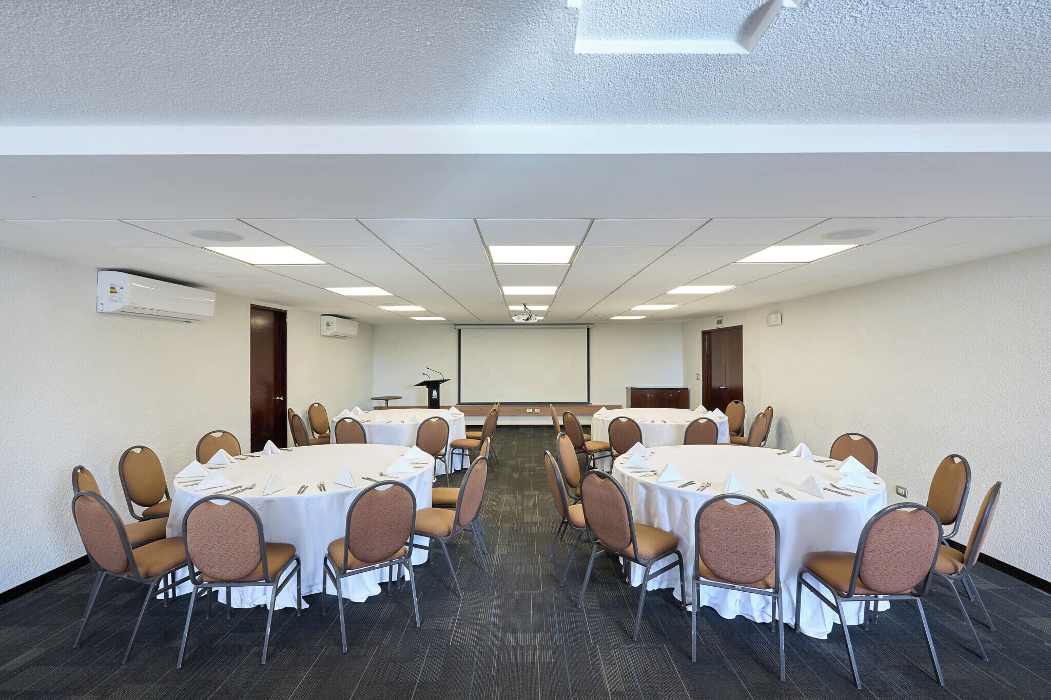 A conference room with round tables, chairs, a projector screen, and a whiteboard.