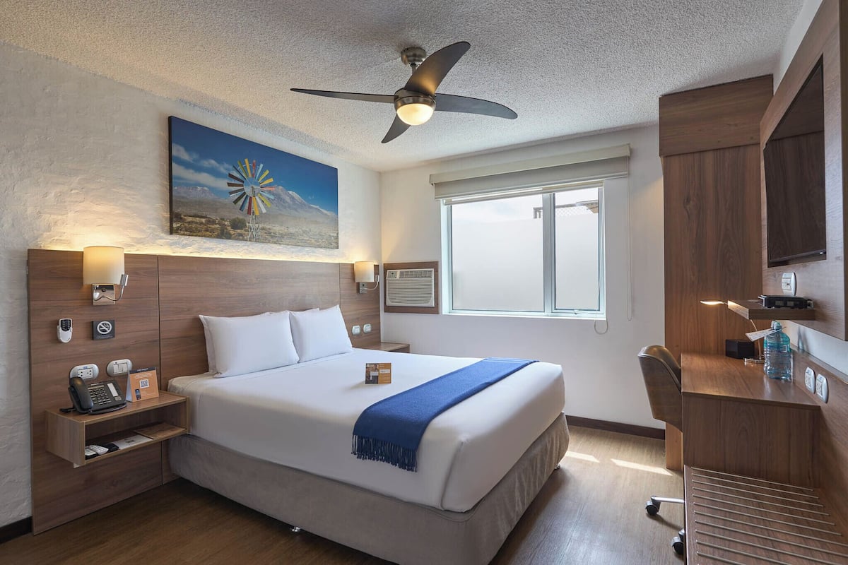 Ein Hotelzimmer mit Bett, Nachttisch, Schreibtisch und Deckenventilator.