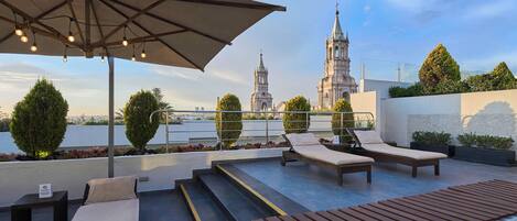 Eine Dachterrasse mit Lounge-Möbeln, Sonnensegel und Blick auf eine historische Kirche.