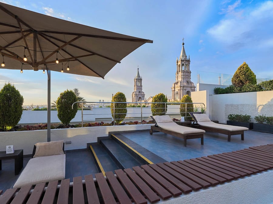 Terraza en la azotea con sillones de descanso, un toldo y vistas a una iglesia histórica.
