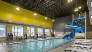 Une piscine intérieure avec un toboggan à eau bleu, des chaises longues et un espace détente avec des tables et des chaises.