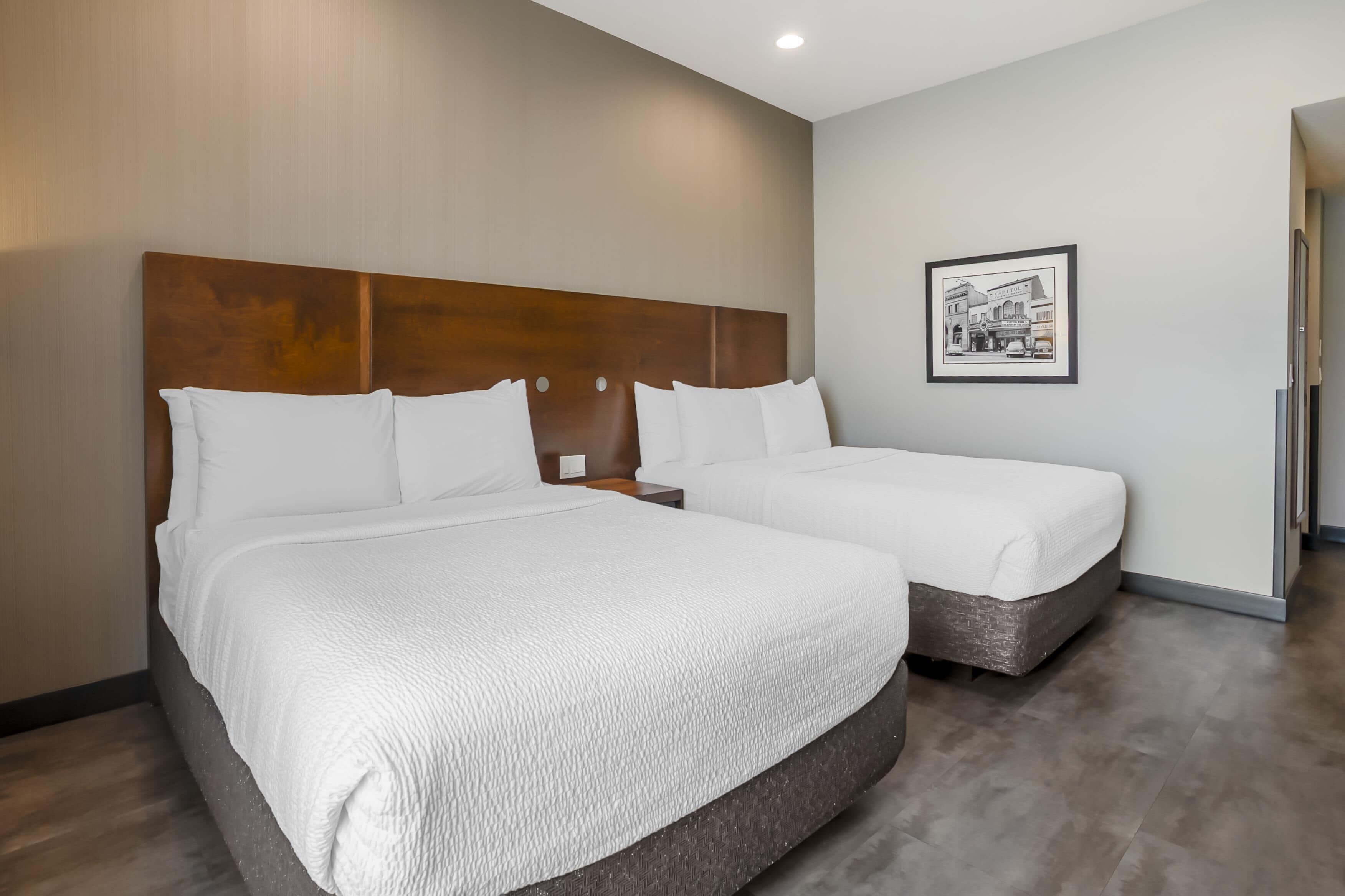 Quarto de hotel com duas camas, cabeceira de madeira, quadro emoldurado na parede e design moderno.