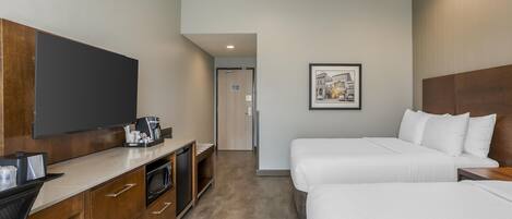 Habitación de hotel con televisión de pantalla plana, cafetera, microondas, mueble de madera, dos camas y un cuadro en la pared.