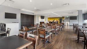 Un grand espace à manger avec plusieurs tables et chaises, une cuisine à l’arrière-plan et un design moderne au niveau du plafond.