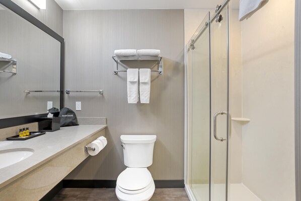 Un baño moderno con inodoro, cabina de ducha de vidrio, toallero con toallas, lavabo y espejo.