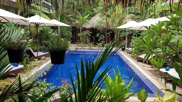 A pool surrounded by lush greenery and white umbrellas, with lounge chairs and potted plants. - Dream Mango Villa (Siem Reap)