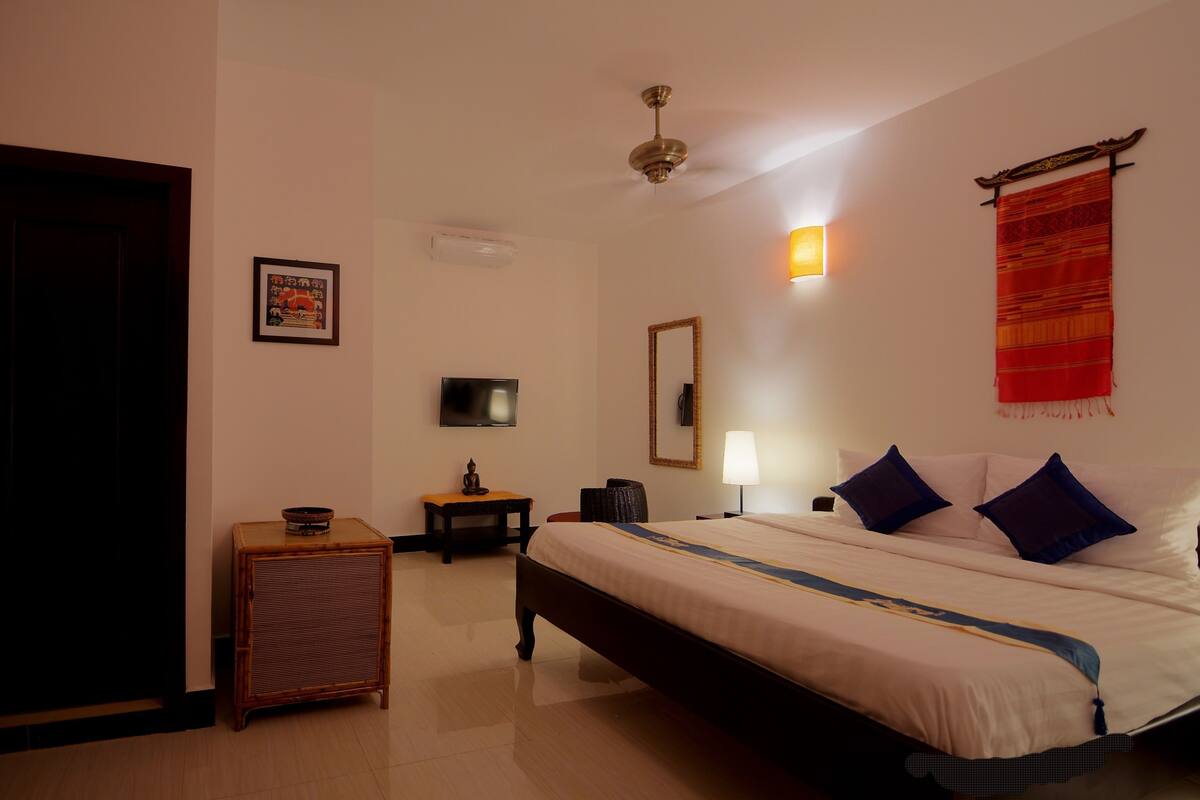 A hotel room with a bed, a television, a small table, a chair, and a decorative wall hanging.