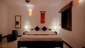 A neatly arranged hotel room with a large bed, two bedside tables, a wall-mounted lamp, a hanging tapestry, and a window with a curtain. - Dream Mango Villa (Siem Reap)