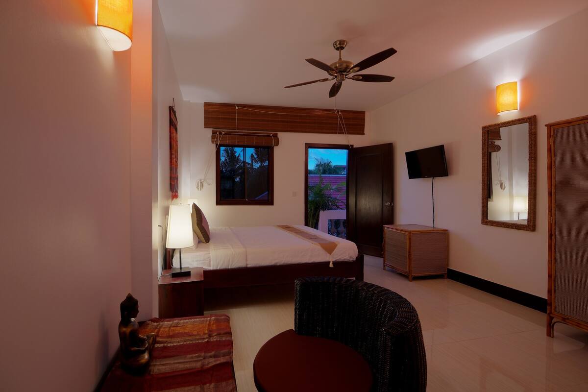 A bedroom with a bed, a ceiling fan, a TV, a mirror, and a window with a view.