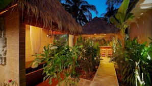 A thatched-roof structure with a pathway leading to a wooden door, surrounded by lush greenery and palm trees. - Dream Mango Villa (Siem Reap)
