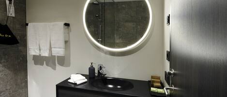 A modern bathroom with a round mirror, black sink, and a towel rack.