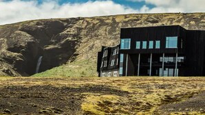Un bâtiment moderne de couleur noire, doté de nombreuses fenêtres, situé dans un paysage aride, avec une colline rocheuse en arrière-plan.
