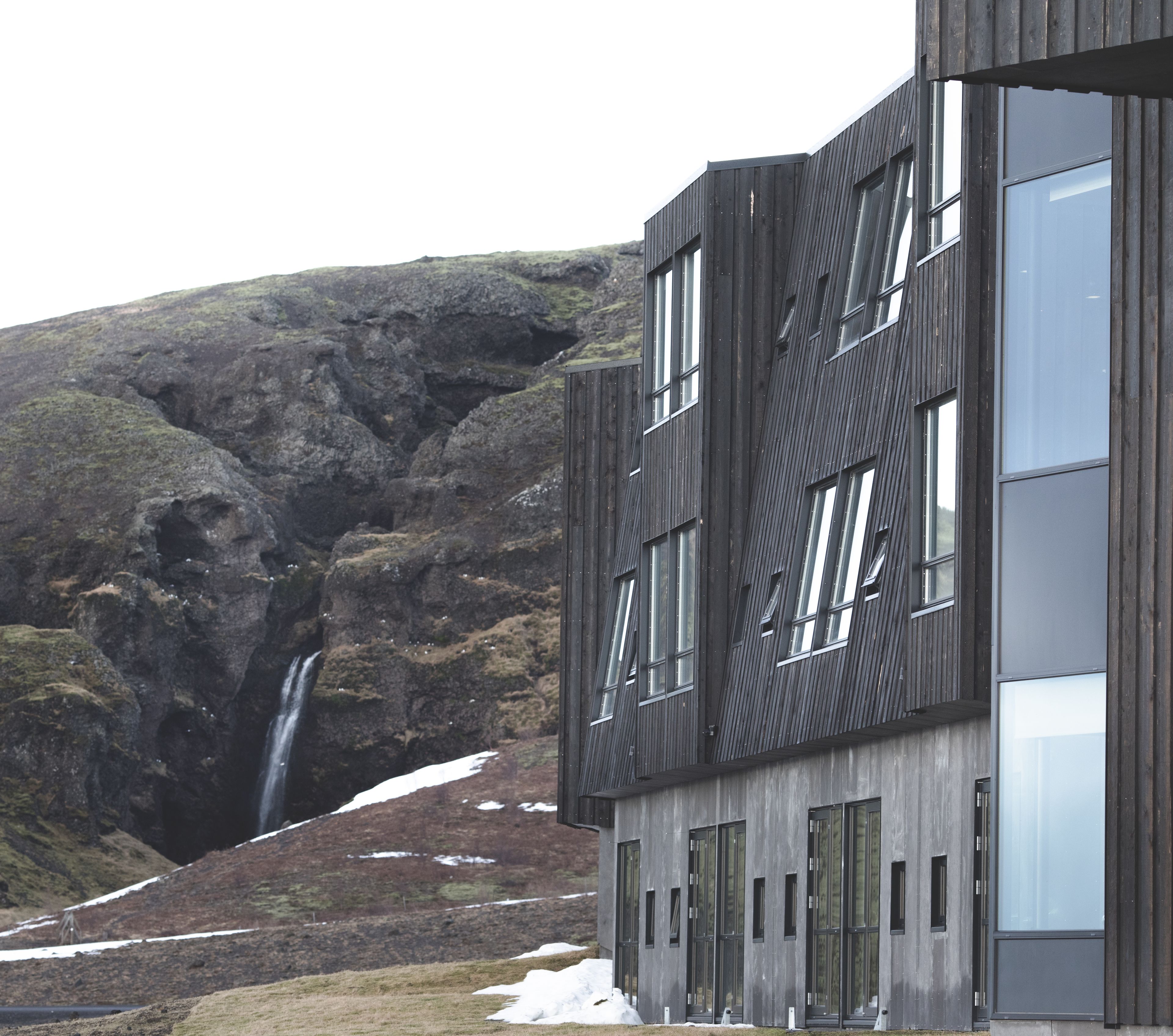 A modern building with a unique architectural design, featuring large windows and a waterfall in the background.