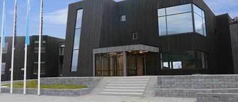 Un edificio moderno con fachada oscura, ventanas amplias y una escalera que lleva a la entrada.