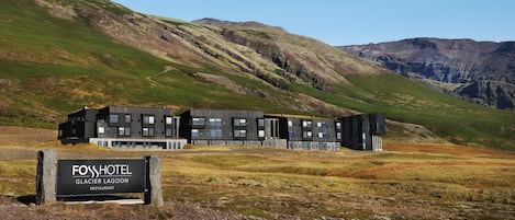 A modern hotel with a sign reading "FOSS HOTEL Glacier Lagoon Restaurant" in a mountainous landscape.