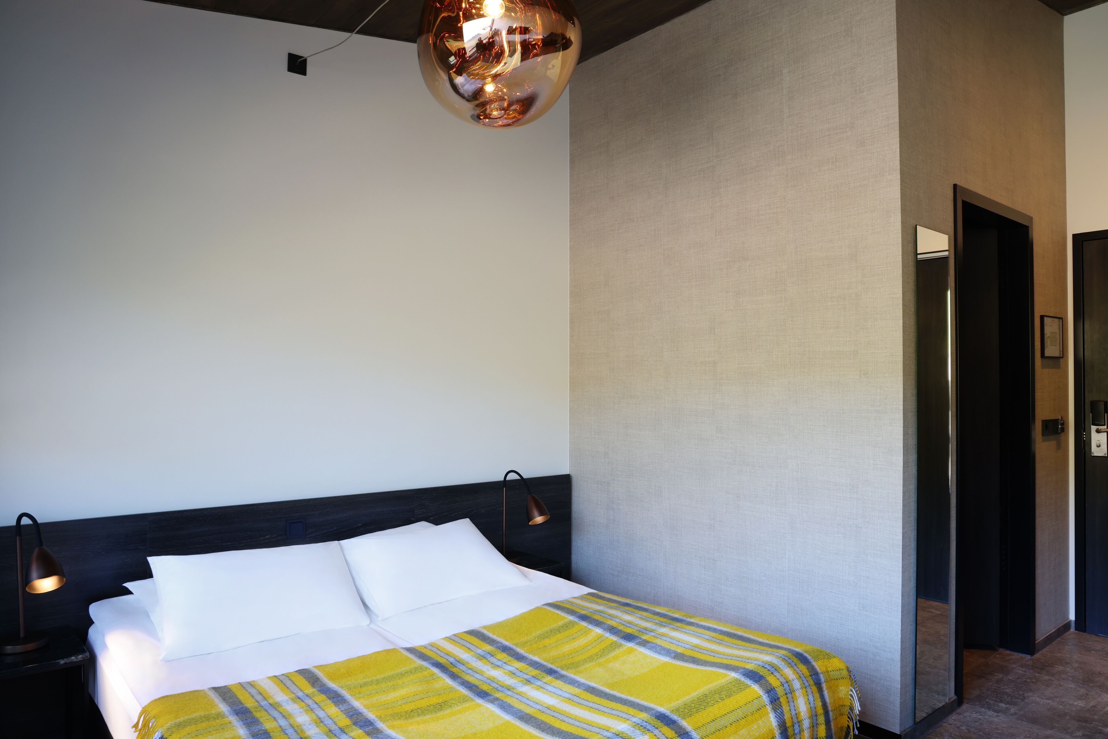 Una habitación de hotel moderna con una cama grande, un cabecero oscuro y una lámpara colgante esférica original.