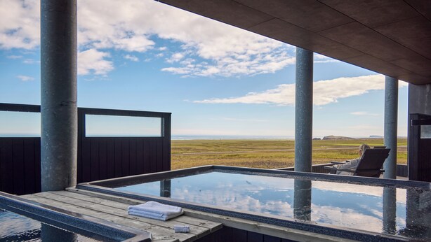 Un bain à remous avec une terrasse en bois et une vue sur un champ verdoyant et des collines lointaines.