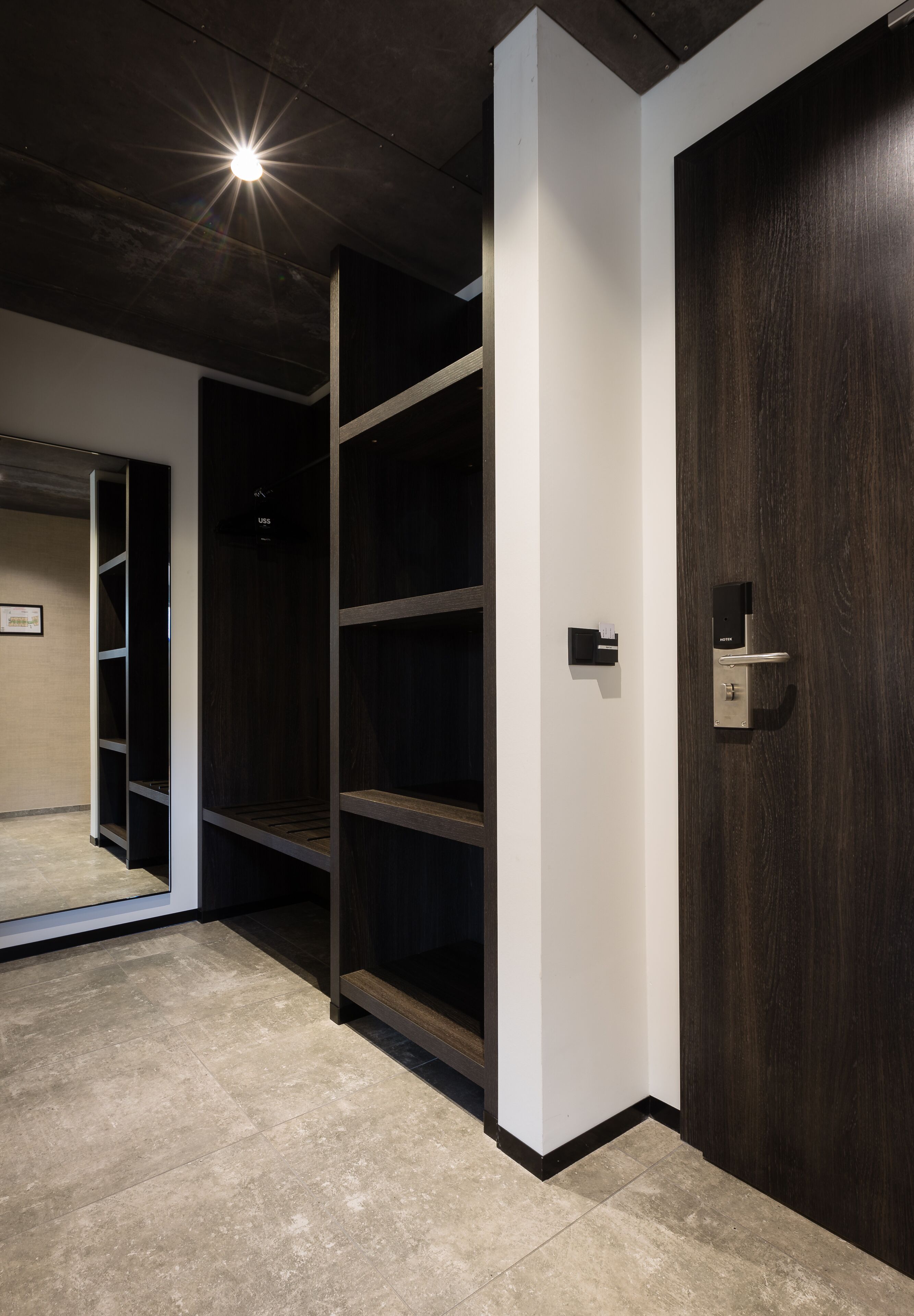 Een modern interieur met een donker houten deur, een witte muur en een metalen plankensysteem.