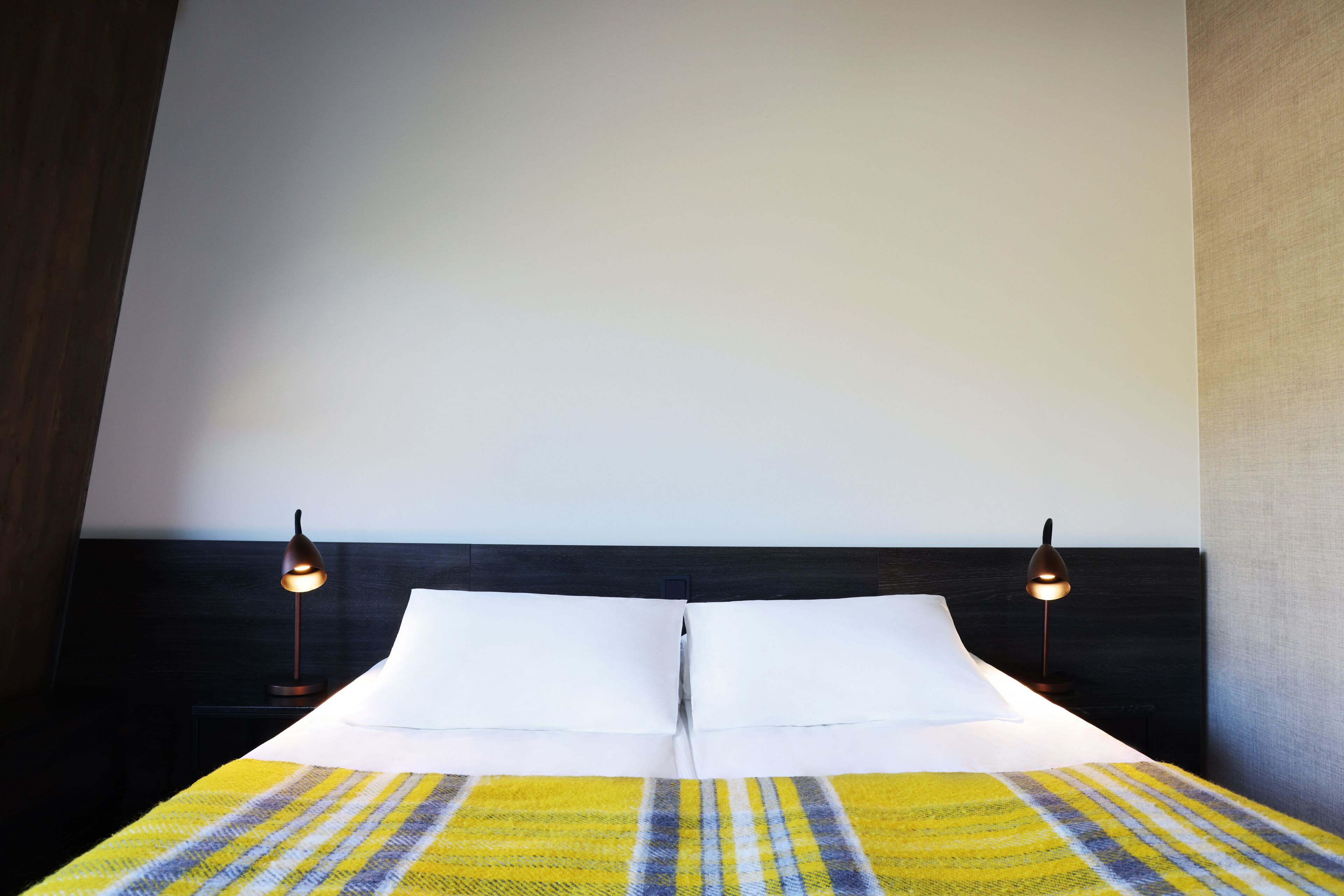 A neatly made bed with white linens and a striped blanket, flanked by two bedside lamps on a dark headboard.