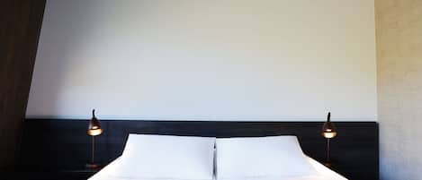 A neatly made bed with white linens and a striped blanket, flanked by two bedside lamps on a dark headboard.