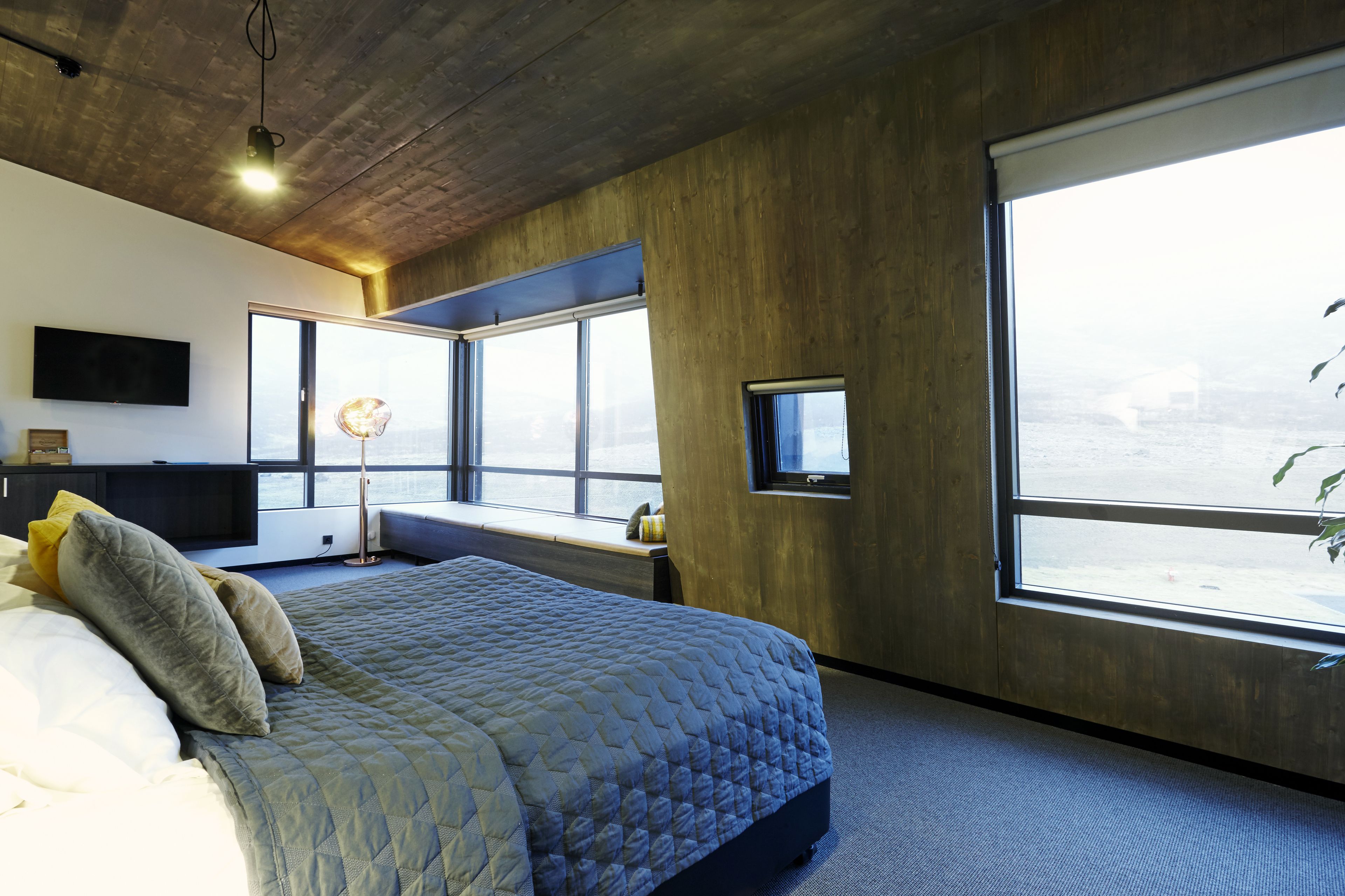 A modern bedroom with a large bed, a desk, and a view of the city through large windows.