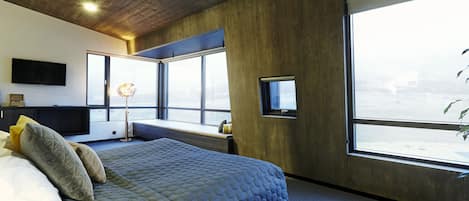 A modern bedroom with a large bed, a desk, and a view of the city through large windows.