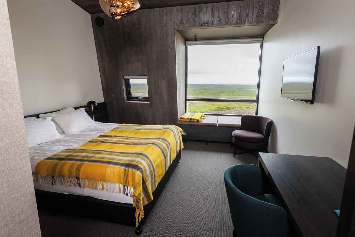 Una habitación de hotel con cama, escritorio, silla, televisor, ventana con vista y un ventanal pequeño.