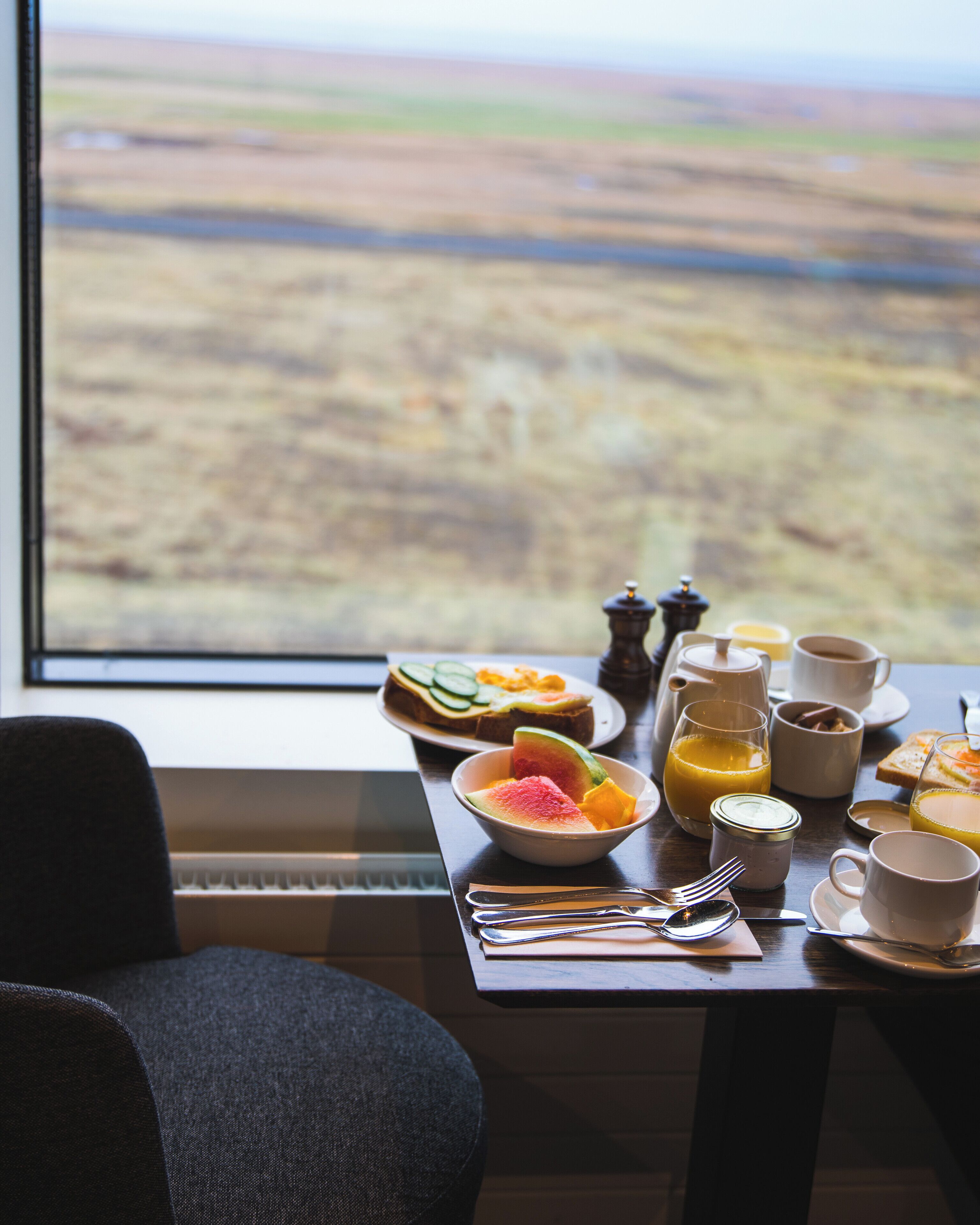 A breakfast table with a view of a landscape through a window.
