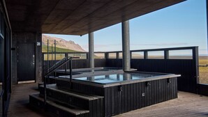 Een hottub onder een houten terras, met uitzicht op een bergachtig landschap.