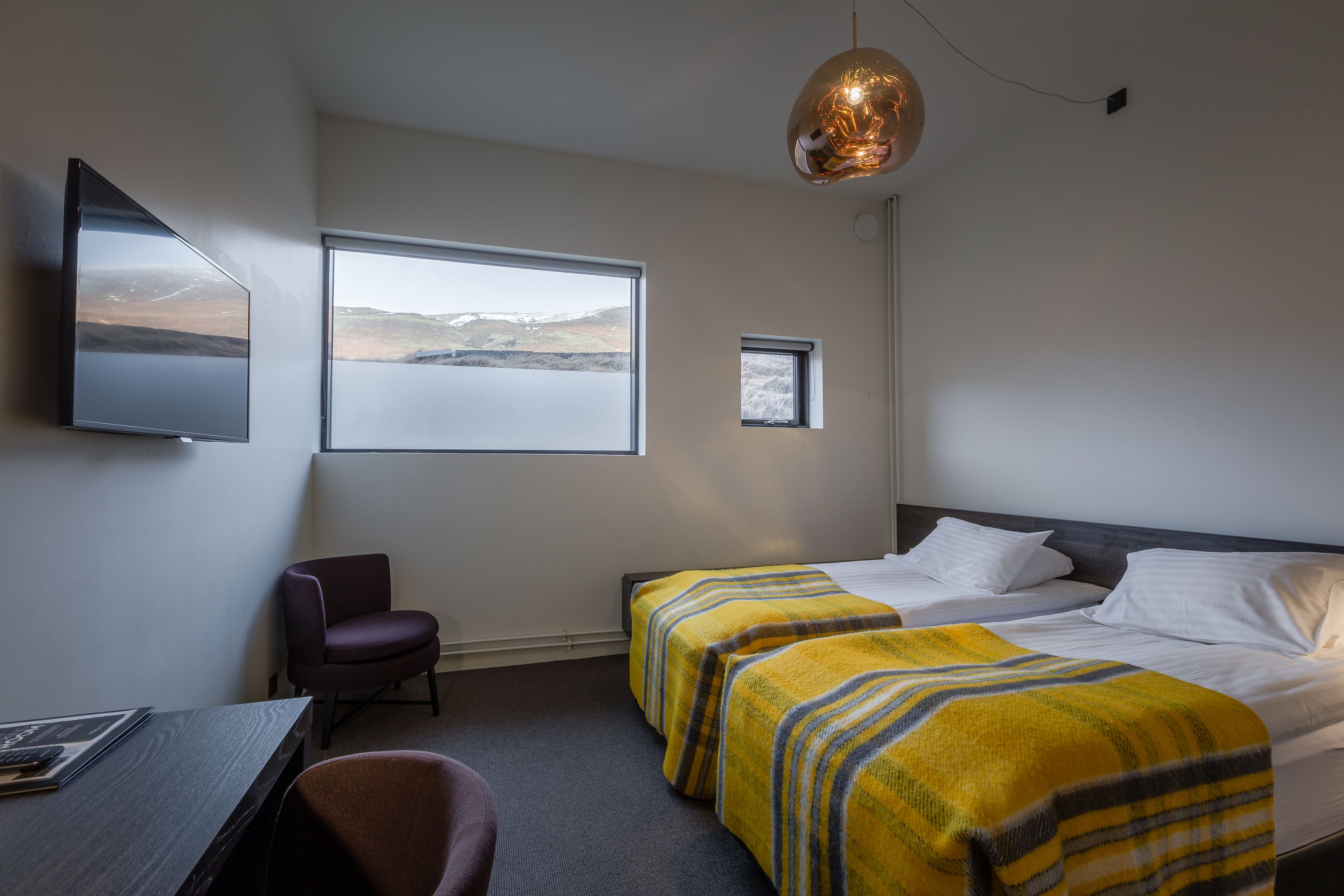 Habitación de hotel con cama, dos mesitas de noche, un escritorio, una silla, televisor y ventana con vistas.