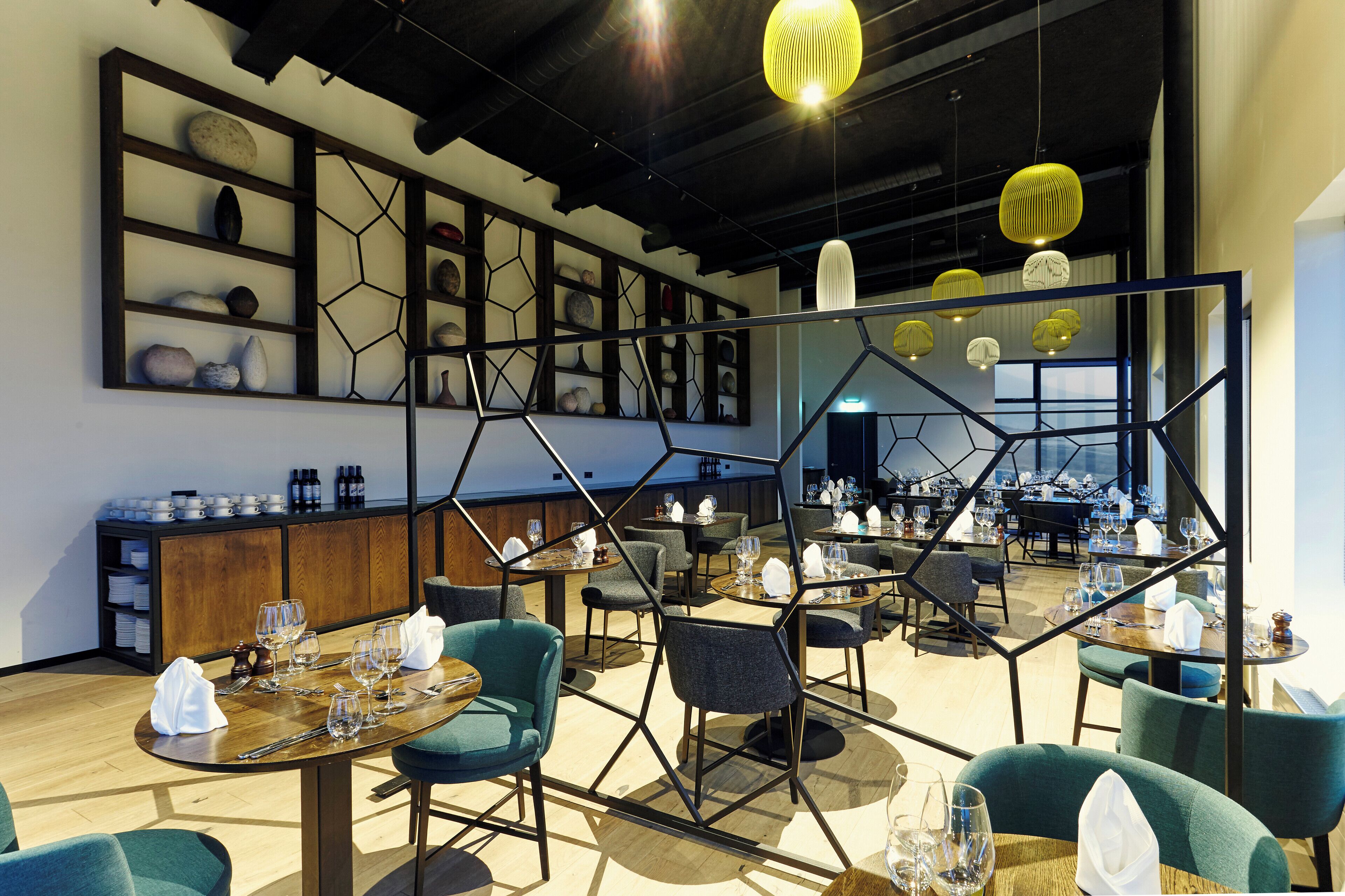 A modern restaurant with hexagonal partitions, wooden tables, and green upholstered chairs.