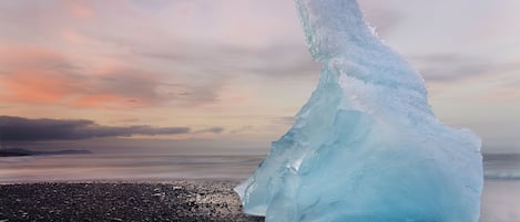 Una gran formación de hielo en una playa, con un mar tranquilo y un cielo nublado.