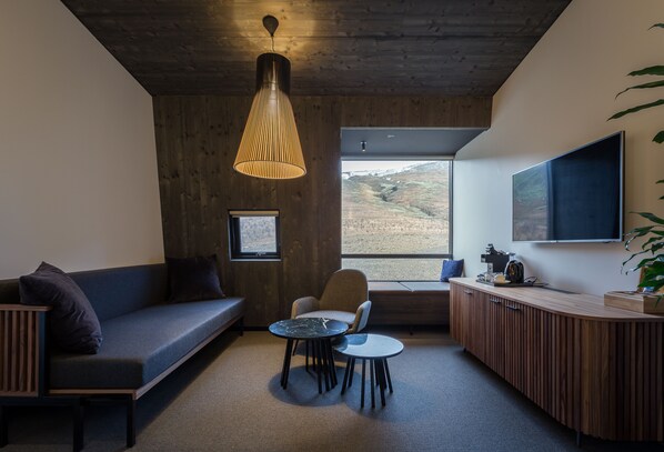 A modern interior with a sofa, two tables, a chair, a wooden cabinet, and a large window offering a view. - Fosshotel Glacier Lagoon (Fagurholsmyri)