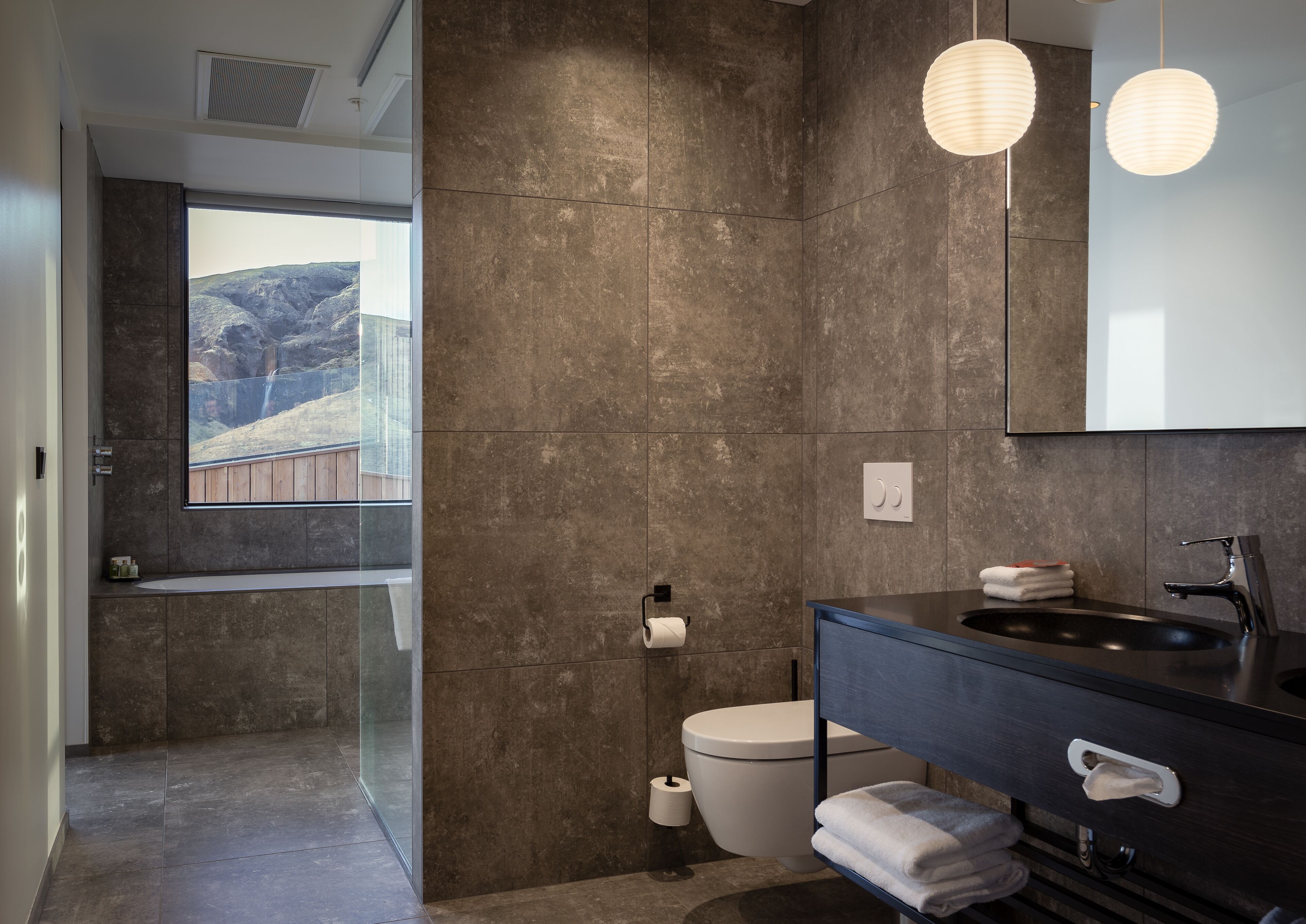 A modern bathroom with a large mirror, a black sink, and a toilet.