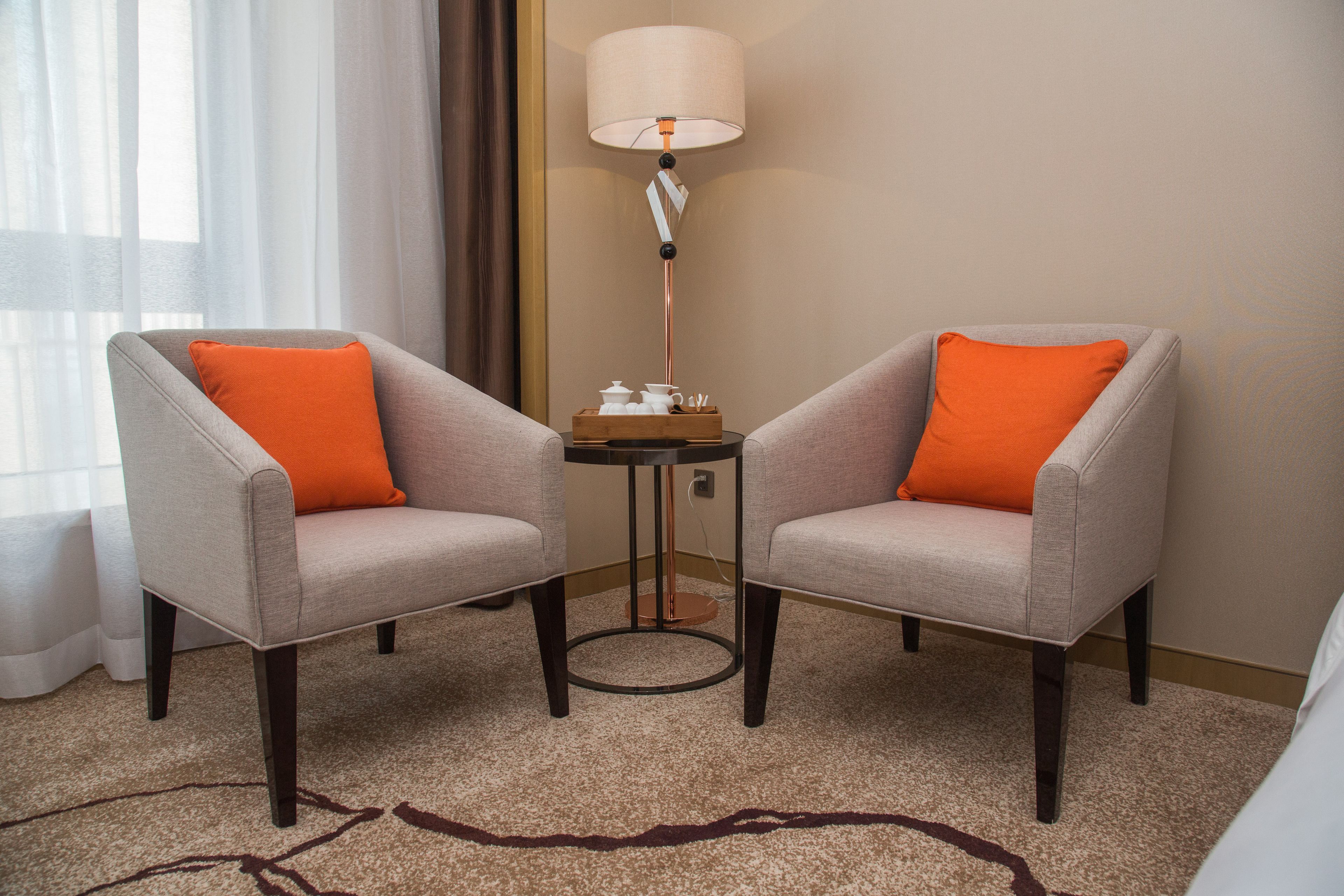 Two armchairs with orange cushions, a small table with a lamp, and a carpeted floor.